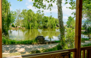 Vista dalla terrazza della Cottage Next XL Loggia Laguna su uno stagno e alberi al Trasimeno Glamping Resort, Italia.