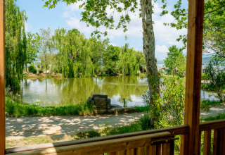 Vista desde la terraza del Cottage Next XL Loggia Laguna hacia un estanque y árboles en Trasimeno Glamping Resort, Italia.