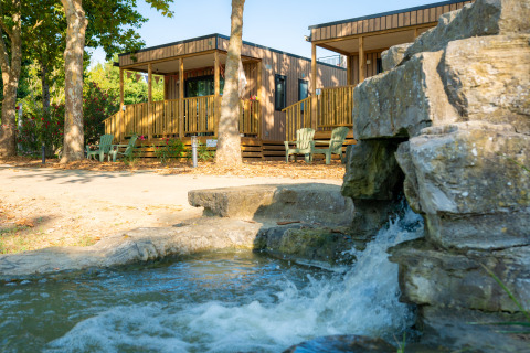 Dos cabañas de madera junto a una cascada y árboles, en Trasimeno Glamping Resort, Italia.