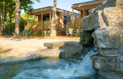 Due cottage in legno accanto a una cascata e alberi al Trasimeno Glamping Resort in Italia.