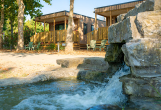 Dos cabañas de madera junto a una cascada y árboles, en Trasimeno Glamping Resort, Italia.