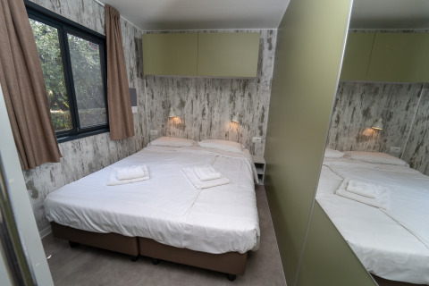 Habitación acogedora en una cabaña con cama doble, pared de espejo, ventana grande y lámparas de noche.