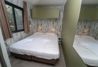 Habitación acogedora en una cabaña con cama doble, pared de espejo, ventana grande y lámparas de noche.