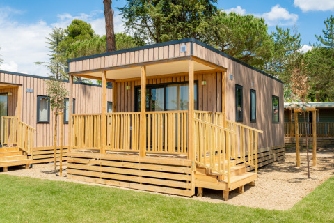 Lodge de madera moderna con porche y barandilla en Cottage Next XL Loggia, rodeada de árboles y césped.