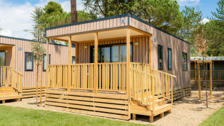 Moderno cottage in legno con veranda e balaustra al Cottage Next XL Loggia, circondato dal verde.