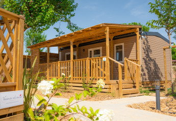 Moderna cabaña de madera Cottage Next XL Mercure con amplia veranda y vegetación en un día soleado.