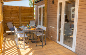 Veranda esterna del Cottage Next XL Mercure al Trasimeno Glamping Resort, con tavolo da pranzo apparecchiato.
