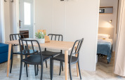 Zona pranzo luminosa con tavolo in legno e sedie nere nel Cottage Next XL Mercure, Trasimeno Glamping Resort.