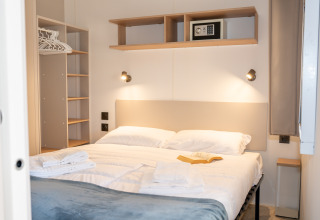 Dormitorio moderno en Cottage Next XL Mercure, Trasimeno Glamping Resort, con cama doble y armario abierto.