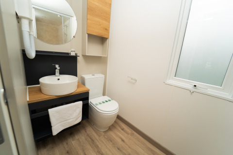 Moderne badkamer met ronde spiegel, wastafel en toilet in de Cube Suite XL bij Trasimeno Glamping Resort, Italië.