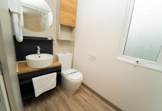 Moderne badkamer met ronde spiegel, wastafel en toilet in de Cube Suite XL bij Trasimeno Glamping Resort, Italië.