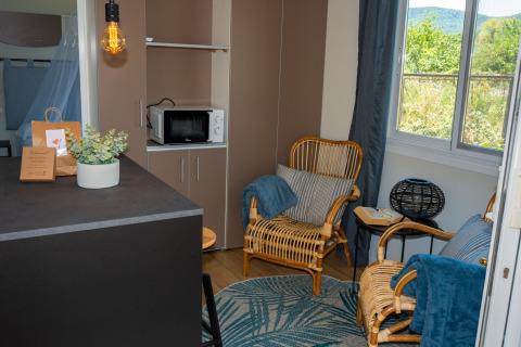 Sala de estar en la suite «Cottage Classic» en Trasimeno Glamping Resort con sillas de mimbre y grandes ventanales.