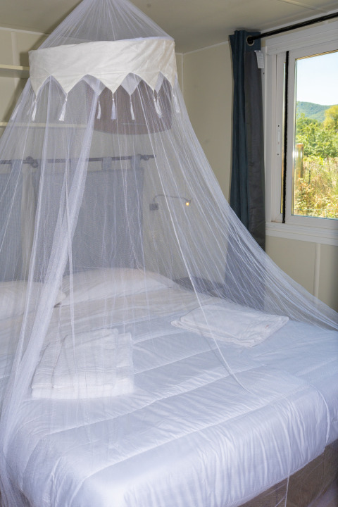 Cama con mosquitera y sábanas blancas en la Suite Cottage Classic de Trasimeno Glamping Resort, Italia.