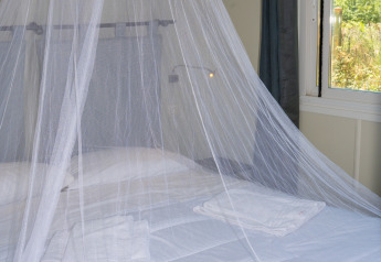Cama con mosquitera y sábanas blancas en la Suite Cottage Classic de Trasimeno Glamping Resort, Italia.