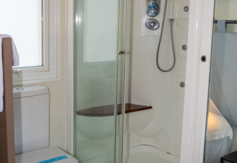Baño moderno con ducha, inodoro y ventana en la Suite Cottage Classic del Trasimeno Glamping Resort en Italia.