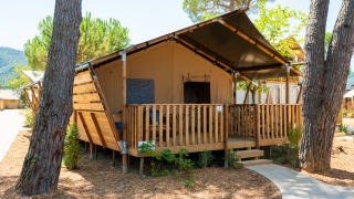 Tenda safari con veranda in legno circondata da alberi in uno scenario naturale e cielo sereno.