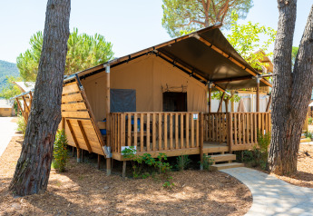 Tienda safari con terraza de madera rodeada de árboles en un entorno natural bajo un cielo soleado.