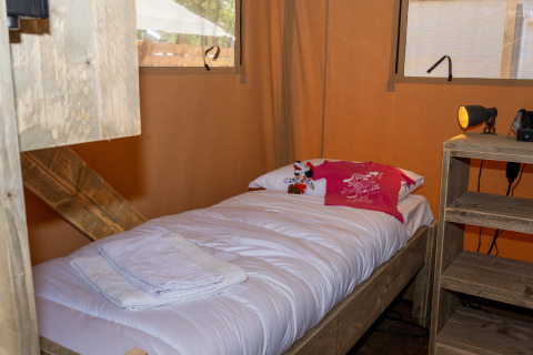 A cozy single bed inside a safari tent, featuring white linens, towels, and a small plush toy.