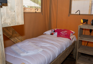 Lit simple confortable dans une tente safari avec draps blancs, serviettes et une peluche sur l’oreiller.