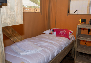 Cama individual acogedora en una tienda safari, con sábanas blancas, toallas y un muñeco de peluche.