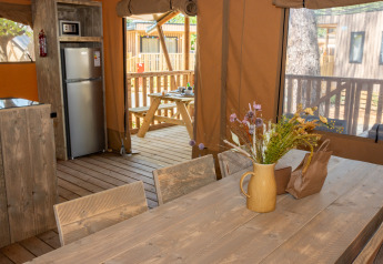 Interior de una tienda safari con muebles de madera, nevera, flores y acceso a una terraza exterior.