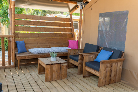 Coin salon confortable sous tente safari avec meubles en bois, coussins colorés et petite plante en pot.
