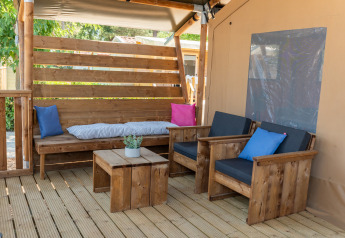Coin salon confortable sous tente safari avec meubles en bois, coussins colorés et petite plante en pot.