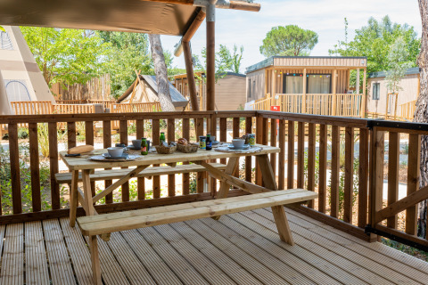 Outdoor terrace with picnic table set for breakfast, overlooking safari tents and cabins in greenery.