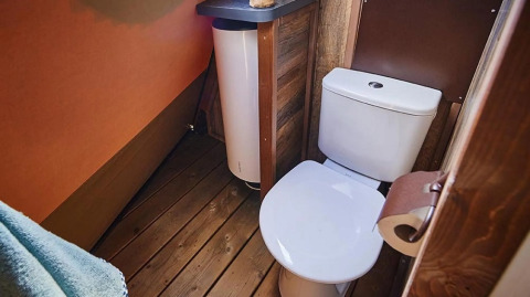 Lichte badkamer met modern toilet en houten vloer in een tipi lodge bij Trasimeno Glamping Resort, Italië.