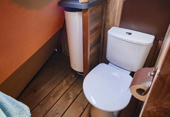 Lichte badkamer met modern toilet en houten vloer in een tipi lodge bij Trasimeno Glamping Resort, Italië.