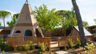 Buitenaanzicht van Tipi Lodge met tipi tent, houten terras en groene omgeving voor een unieke ervaring.
