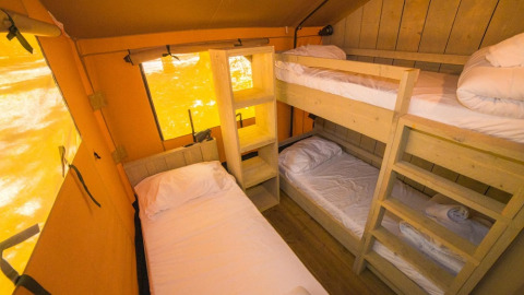 Binnenzicht van een safaritent met stapelbedden en een eenpersoonsbed in Spotty Lodge Ranger, Trasimeno Glamping Resort, Italië.