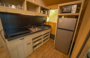 Angolo cucina nella tenda safari al Trasimeno Glamping Resort in Italia con frigo, microonde e fornelli.