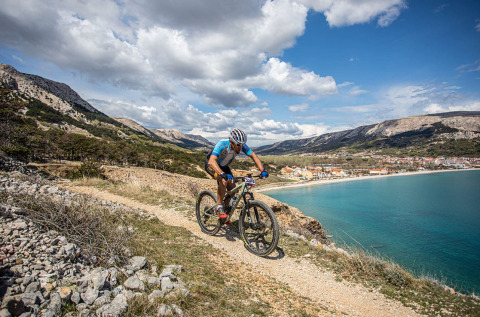 Un ciclista percorre un sentiero costiero con vista panoramica su Baška e il mare azzurro in Croazia.
