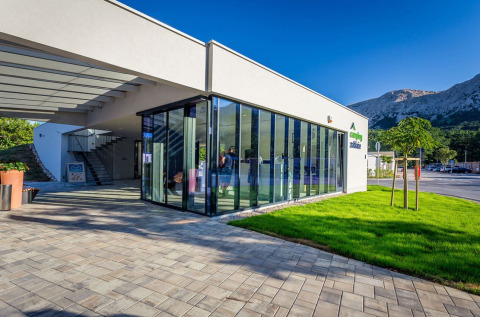 Modern glass entrance and green lawn at Campsite Baška, Primorje-Gorski Kotar County, Croatia, with mountains.