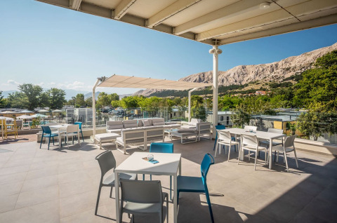 Terrazza esterna al campeggio Baška con tavoli, sedie e vista sulle montagne e la natura circostante.