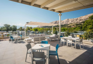 Outdoor terrace at Campsite Baška featuring tables, chairs, comfy seating, and stunning mountain views.