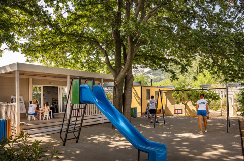 Parco giochi con scivolo e bambini sotto gli alberi al campeggio «Baška» a Primorje-Gorski Kotar, Croazia.