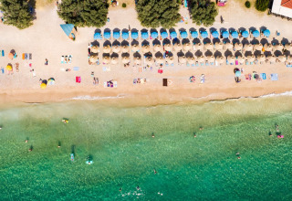 Aerial view of the beach with umbrellas and swimmers at Campsite Baška, Primorje-Gorski Kotar, Croatia.