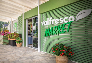 Entrance of Valfresco Market at Campsite Baška with green facade and vibrant flowers in Croatia.