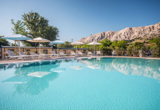 Outdoor pool with loungers and umbrellas at Campsite Baška in Croatia, mountains and clear blue sky seen behind.