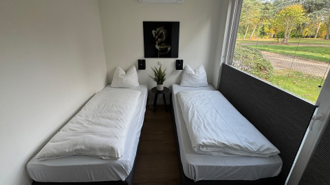 Twee eenpersoonsbedden in een moderne kamer van Forest Lodge, Holiday Park BreeBronne met tuinzicht.