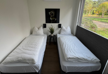 Zwei Einzelbetten im modernen Zimmer der Forest Lodge im Holiday Park BreeBronne mit Blick ins Grüne.