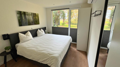 Moderne slaapkamer in Forest Lodge van Holiday Park BreeBronne, met grote ramen en zicht op de tuin.