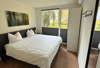 Moderne slaapkamer in Forest Lodge van Holiday Park BreeBronne, met grote ramen en zicht op de tuin.