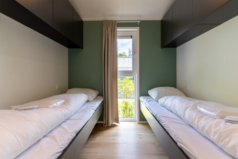 Twee eenpersoonsbedden in een moderne kamer met groene muur, kasten en raam in Wellness Cottage.