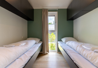 Two single beds in a modern room with green accent wall, overhead cabinets, and window in Wellness Cottage.