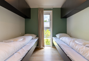 Zwei Einzelbetten in einem modernen Zimmer mit grüner Wand, Schränken und Fenster in Wellness Cottage.