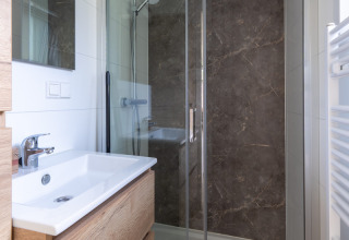Moderne badkamer in een huisje met houten wastafelmeubel, glazen douche en marmeren wand bij De Thijmse Berg.