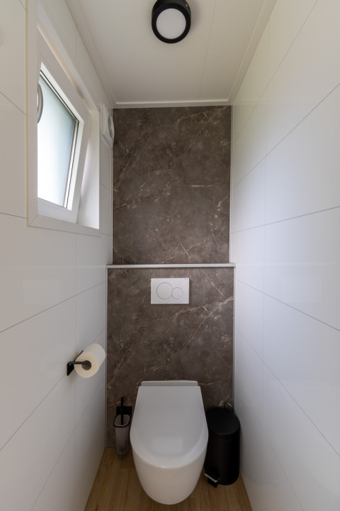 Baño moderno y estrecho con inodoro, ventana y pared de mármol en Wellness Cottage, De Thijmse Berg, Países Bajos.